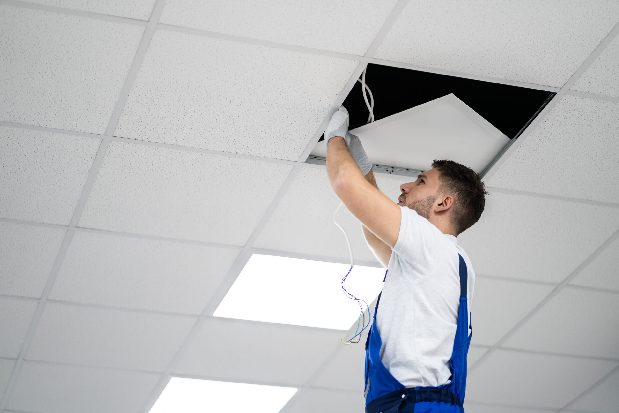 Full Length Portrait Of Electrician On Stepladder Installs Lighting To The Ceiling In Office